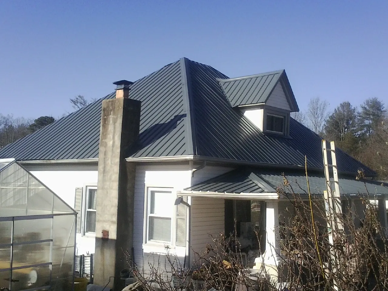 Dark blue standing seam metal roof on a white farmhouse with dormer — Slate & Tile Roof Repair by Roofing Brothers in Drexel