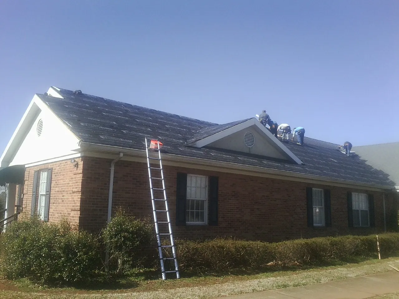 Crew tearing shingles off a brick ranch roof with a ladder set — Metal Roof Repair work by our crew in Drexel