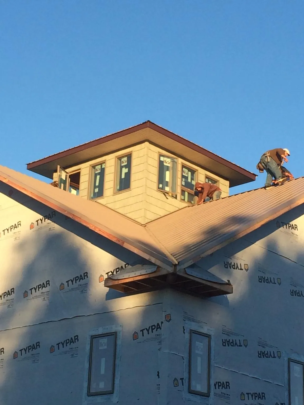 Roofers working around a rooftop cupola on a new metal roof at sunset — Roof Waterproofing in Drexel by Roofing Brothers
